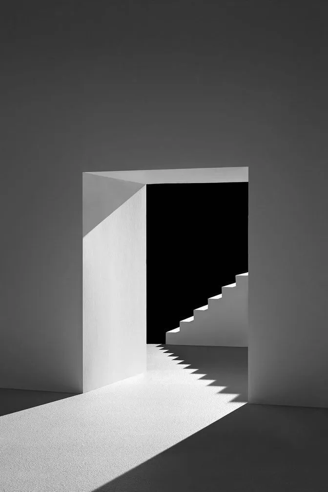 Minimalist white doorway opening onto a staircase washed in dramatic light
